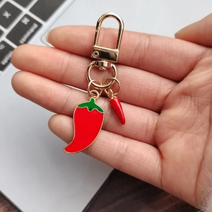 Close-up of a 3D red chili pepper keychain with golden swivel clasp on a laptop background