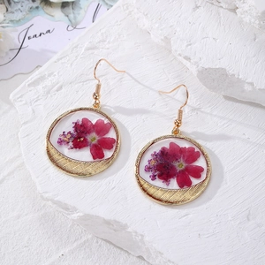 Detailed close-up of golden floral earrings with real dried flowers on white stone