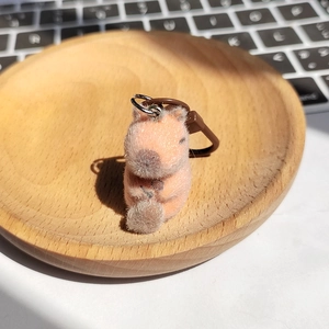 Dettaglio di un simpatico portachiavi a forma di capibara arancione su un piatto di legno