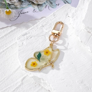 Detailed close-up of golden butterfly keychain with real dried flowers in resin