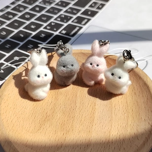 Close-up of four colorful flocked bunny keychain pendants in a wooden tray on a desk