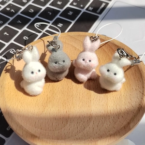 Close-up of four soft flocked rabbit pendants in white, pink and grey on a wooden tray
