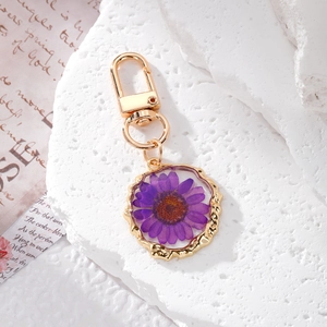 Handmade gold keychain with purple dried daisy flower in resin on a white stone background