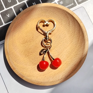 Detail shot of a double cherry keychain with a golden heart clasp on a wooden tray