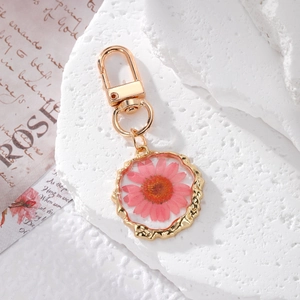 Detailed macro shot of a pink dried daisy flower resin keychain with golden metal frame