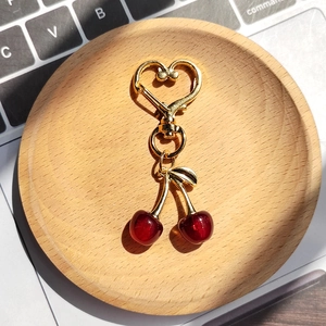 Detailed view of resin cherry keychain with heart shaped gold clasp and red fruit