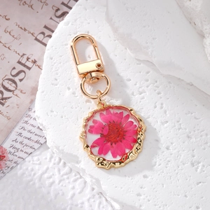 Detail view of pink dried daisy flower embedded in gold resin circle keychain charm