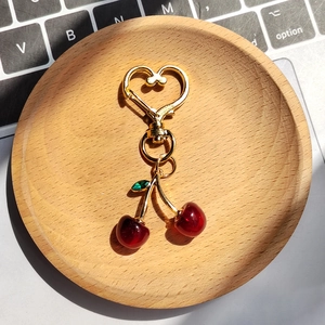 Realistic cherry heart keychain with red resin fruit and golden metal frame on wood