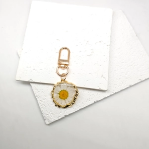 Close-up of white daisy dried flower resin keychain with golden wavy edge detailing