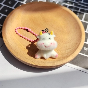 Cute white flocked cow keychain with pink bead chain on a wooden tray over a keyboard