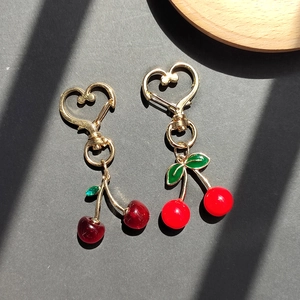 Detail of red resin cherry keychains with green leaves and gold heart-shaped metal hooks