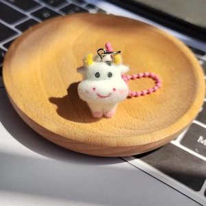 Cute flocked cow animal keychain with pink bead chain on a wooden tray for bags and phones