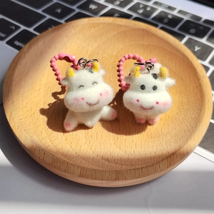 Close-up of two cute flocked cow keychains with pink bead chains on a wooden tray
