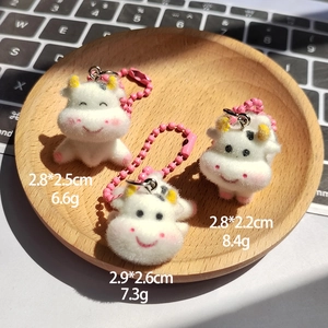 Detailed view of three cute flocked cow keychains with dimensions and weights on a wooden tray