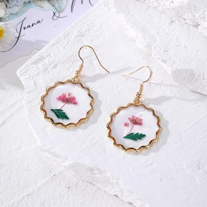 Handmade gold earrings with pink dried flowers in round wave frames on white stone