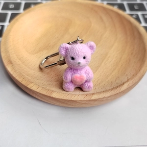 Cute purple flocked teddy bear keychain with pink heart on a small wooden tray