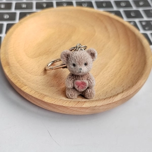 Cute brown flocked bear plush keychain with red heart on a decorative wooden tray