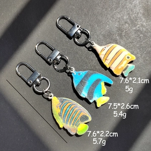 Three colorful flocking tropical fish keychains with metal lobster clasps on black surface
