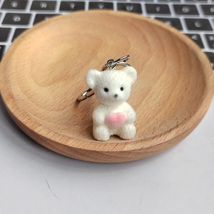 Close-up of a cute white plush bear keychain holding a pink heart in a wooden tray