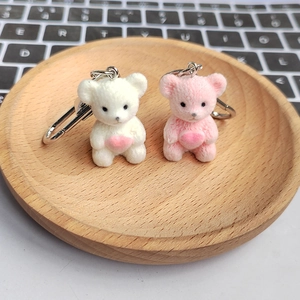 Cute flocked teddy bear keychains in pink and white holding hearts in a wooden tray