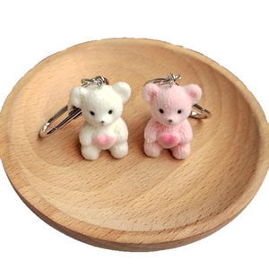 Cute flocked teddy bear keychains in pink and white holding hearts on wooden tray