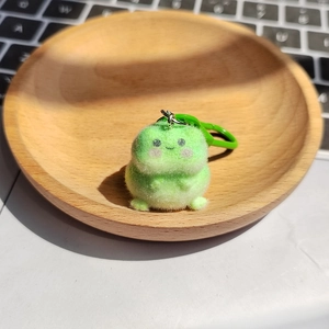 Porte-clés grenouille en peluche verte sur un plateau en bois avec décor de bureau