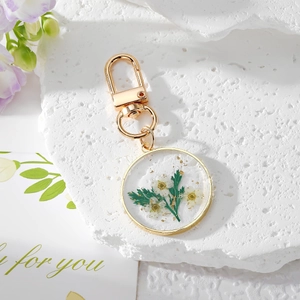 Floral resin keychain with white dried flowers and gold foil in a round metal frame