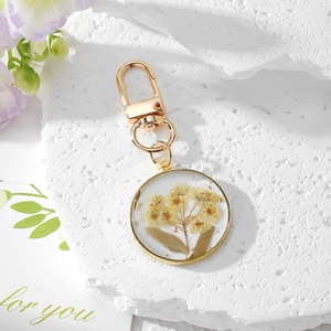 Detail of round gold pendant keychain with real yellow dried flowers in clear resin