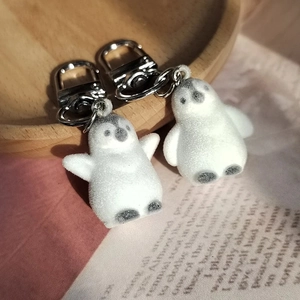 Pair of cute flocked penguin keychains with silver metal hooks on a rustic wooden tray