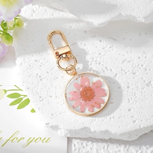 Detailed macro view of handmade pink daisy resin keychain with gold leaf on textured rock