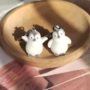 Close-up of two cute flocked penguin keychains on a wooden tray with soft lighting
