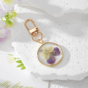 Detail of round resin keychain with yellow purple dried flowers and gold foil accents