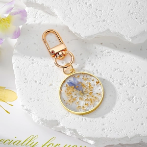 Detail of round resin keychain with blue dried flowers and gold foil on white stone