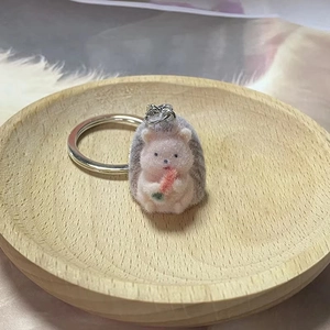 Cute pink and grey flocked hedgehog keychain with a carrot on a wooden tray