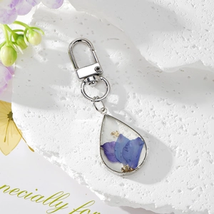Dettaglio del portachiavi a goccia d'argento con fiori secchi blu e foglia d'oro vera
