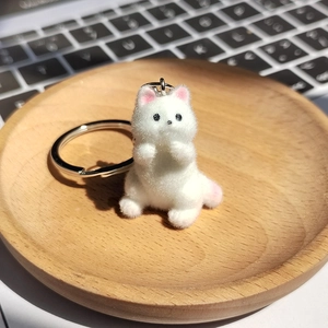 Porte-clés chat blanc en peluche floquée présenté dans un plateau en bois décoratif