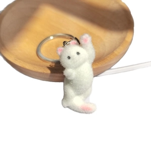 Porte-clés chat blanc floqué avec oreilles roses sur un plateau en bois naturel