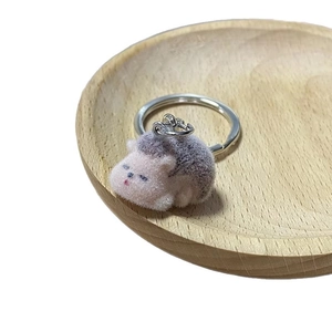 Cute pink flocked hedgehog plush keychain with purple fur and silver keyring on wood tray