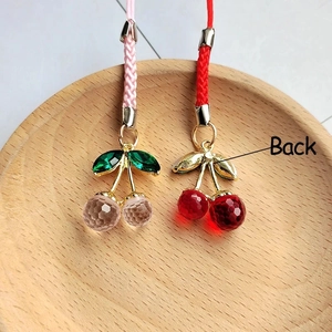 Close-up of handmade resin cherry pendants with faceted beads on a wooden tray