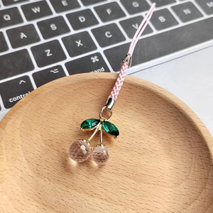 Pink resin cherry keychain with faceted crystal beads and green leaves on wooden plate