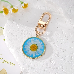 Détail macro d'un porte-clés marguerite ronde en résine avec bordure dorée et fond bleu