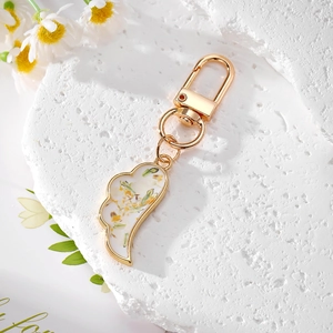 Golden wing keychain with dried flowers and petals on white stone display