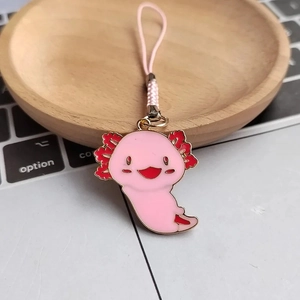 Pink axolotl alloy keychain with woven strap on wooden tray near laptop keyboard