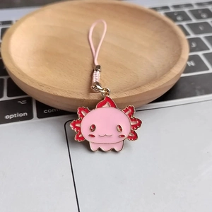Pink axolotl charm with pink braided cord on a laptop and wooden surface