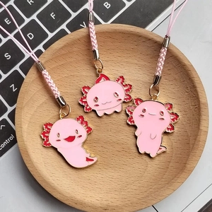 Detailed view of three pink axolotl enamel charms with woven lanyards on wooden tray
