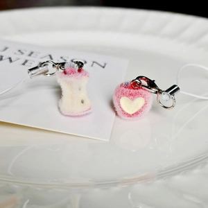 Detail of plush apple core and heart charms with silver lobster clasps on a white tray