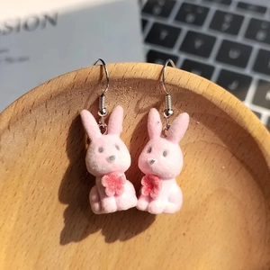 Close-up of pink flocked rabbit earrings with red flowers hanging on a wooden bowl