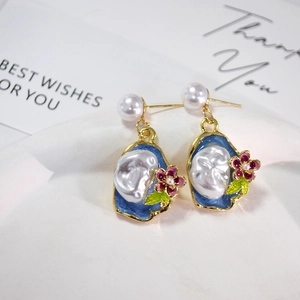 Detail shot of vintage pearl earrings with blue enamel and floral accents on ceramic plate