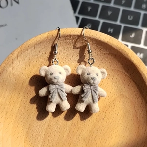 Close-up of cute grey flocked bear earrings with bow details on a wooden tray