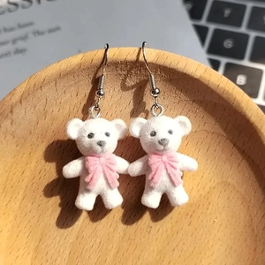 Cute white flocked bear earrings with pink bow ties on a wooden tray setting